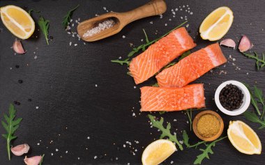 Saf somon fileto, deniz tuzu, limon ve biber ile siyah taş arka planda. Pişirmeye hazır taze balık. Üst görünüm, boşluğu kopyala. Sağlıklı Beyin Gıda Konsepti.