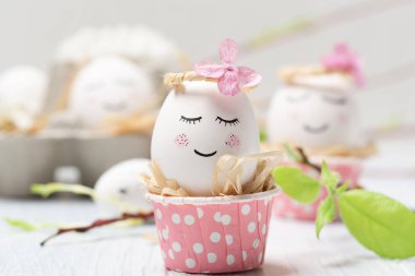 Beyaz şirin yumurtalar, ağaç dalları, bıldırcın tüyleri ve beyaz ahşap arka planda bahar çiçekleri olan tatil yaratıcı Paskalya konsepti. Seçici odak, uzayı kopyala. Paskalya bayramı tebrik kartı..