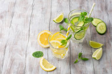 Taze meyve, limonata içecekler, serinletilmiş su. Taze limonlu, salatalıklı, limonlu ve naneli bardaklar. Beyaz tahta arkaplan, boşluğu kopyala.