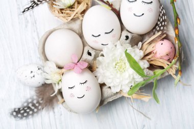 Beyaz şirin yumurtalar, yeşil ağaç dalları, bıldırcın tüyleri ve beyaz ahşap arka planda bahar çiçekleri olan sıfır atık Paskalya konsepti. Üst görünüm, boşluğu kopyala. Paskalya bayramı tebrik kartı..