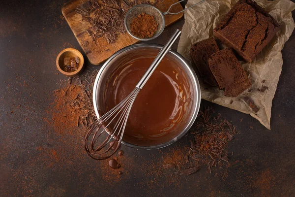 Homemade delicious chocolate vegan cake and sauce in bowl with whisk on dark wooden background. Top view, copy space. Super brain food, vegan baking concept.