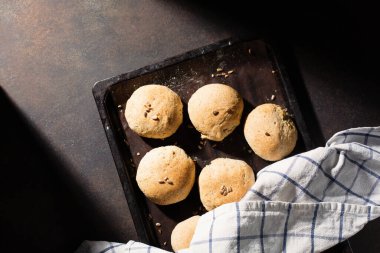 Ev yapımı çavdar ekmekli çörekler, ahşap masa üzerinde tohumlar, koyu rustik arka plan. Üst görünüm, boşluğu kopyala. Alternatif el yapımı yemek pişirme konsepti.