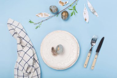 Bayramlık Paskalya sofrası hazırlama geçmişi. Boş tabakla Paskalya süslemesi, mavi altın yumurta, mavi masada bıldırcın tüyü. Paskalya kartı konseptin kutlu olsun. Boşluğu kopyala, üst görünüm.