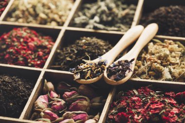 Farklı türde kuru çay. Yeşil, siyah, nane, gül ve papatya çayı, kutuda tahta kaşıklar. Çay zamanı konsepti, sağlıklı içecek..