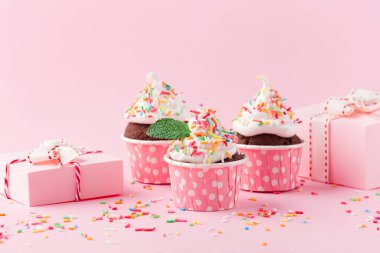 Doğum günü, kadın ya da anneler günü için bayram kekleri. Pembe kağıt süslemeler, üzerine şeker serpiştirilmiş çikolatalı kekler ve pembe arka planda hediye kutuları. Parti zamanı kavramı.