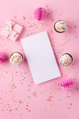 Doğum günü, kadın ya da anneler günü için bayram tebrik kartı. Boş beyaz, hediye kutusu, kağıt süslemeler ve pembe serpiştirilmiş kekler. Düz konum, üst görünüm, kopyalama alanı.