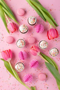 Doğum günü, kadın ya da anneler günü için bayram tebrik kartı. Taze lale çiçekleri, kağıt süslemeler, tatlı kurabiyeler ve pembe serpiştirilmiş kekler. Düz yatış, üst görünüm.