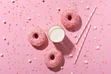 Ulusal Çörek Günü konseptiniz kutlu olsun. Pembe kremalı çörekler, pembe arka planda bir bardak süt ve şeker serpiştirilmiş. Üst görünüm, alanı kopyala.