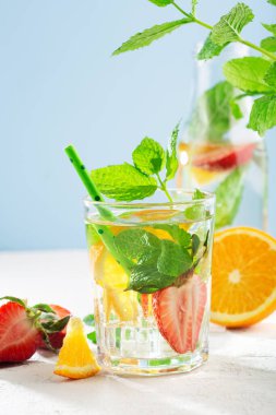 Taze meyve, limonata içecekler, serinletilmiş su. Bir bardak taze çilekli, portakallı, limonlu ve naneli su. Beyaz güneş arkaplanı, kopyalama alanı.