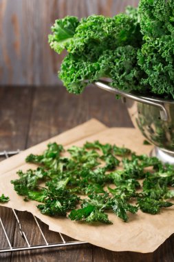 Kırsal ahşap arka planda, zeytinyağı ve deniz tuzu ile ev yapımı çıtır lahana cipsi. Seçici odak, boşluğu kopyala. 