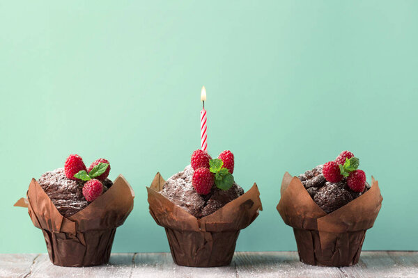 Вкусные шоколадные кексы со свежей малиной и свечами на зеленом мятном фоне. Выборочный фокус, копировальное пространство. Летняя вечеринка.