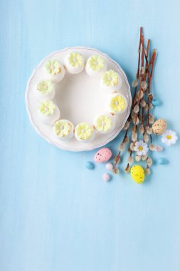 Paskalya bayramı kartı. Neşeli tavşan, boyalı yumurta, söğüt dalları, bahar çiçekleri, açık mavi arka planda dekoratif elementler.