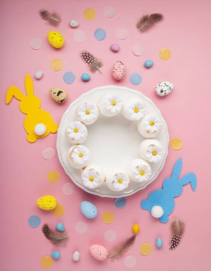 Paskalya bahar tatili sofrası. Beyaz tabak, yumuşak tavşan, boyalı yumurta, açık pembe arka planda bahar çiçekleri. Şenlikli yemek sahnesi