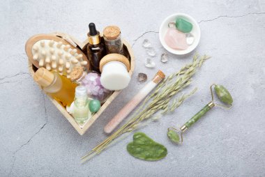 Yeşil yeşim taşlı spa seti, gua sha, yüz yağı, kehribar şişesi, gri taşlı arka planda çevre dostu ambalaj..