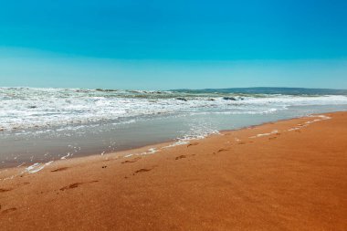 Kumsal kıyısı. Sarı kumdaki mavi dalgalar ve ayak izleri. Kaygısız yaz zamanı. dinlenme ve tatil