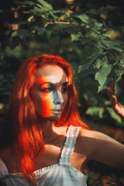 Gökkuşağı suratlı. Gökkuşağı renkleri güzel bir kızıl kızın yüzüne yansıyor. Orman arkaplanı