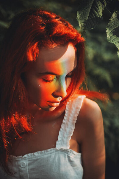 Rainbow face. Rainbow colors reflected on a beautiful redhead girl's face. Forest background