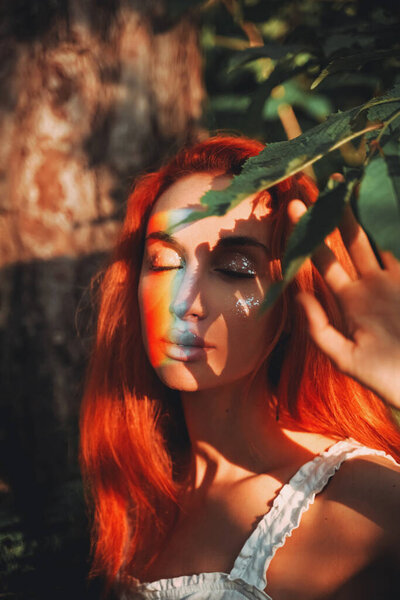 Rainbow face. Rainbow colors reflected on a beautiful redhead girl's face. Forest background