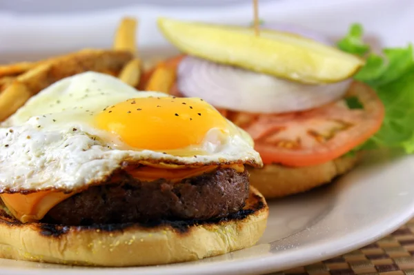 Burger mit Spiegelei, Käse, Tomaten, Zwiebeln und Essiggurke serviert mit frisch geschnittenen Pommes frites — Stockfoto