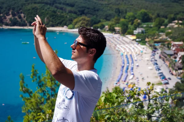 Fiatal férfi tartsa a mobiltelefon, kép nyári strand. — Stock Fotó