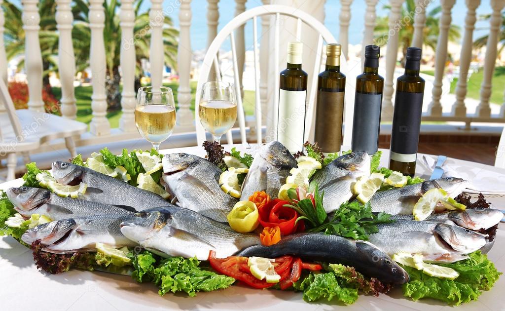 Big plate with fresh fish with vegetables, white wine and olive 