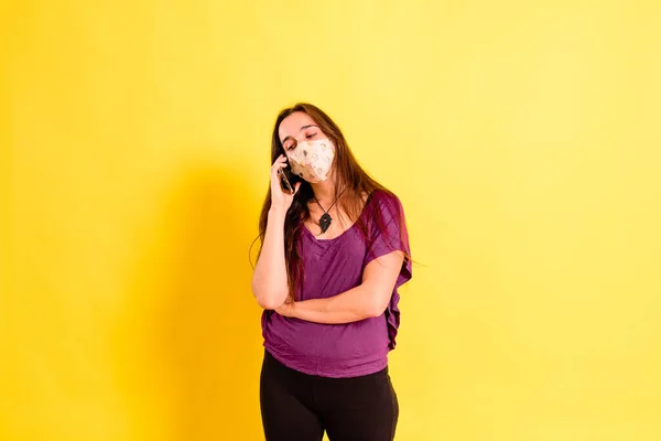 一位年轻女子带着面具拿着智能手机 在黄色的工作室背景下孤立无援 — 图库照片