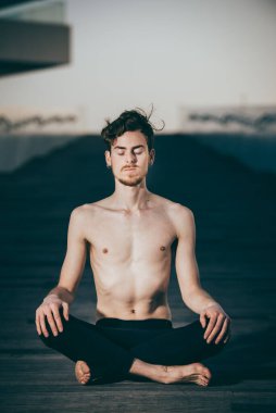 Genç kızıl saçlı adam nilüfer yogası yapıyor, Padmasana, açık havada, ahşap zeminde.