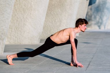 Genç kızıl saçlı erkek sporcu esnek olmak ve kaslarını gevşetmek için antrenmandan sonra esneme hareketleri yapıyor..