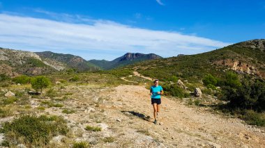 Gerçek görünümlü orta yaşlı bir kadın dağ yolunda koşuyor..