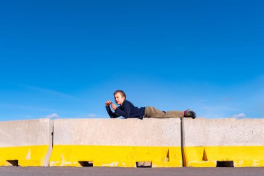 Bir çocuk tehlikeyle karşı karşıya kalan bazı inşaat engelleri üzerinde oynuyor, izole edilmiş mavi arka plan.