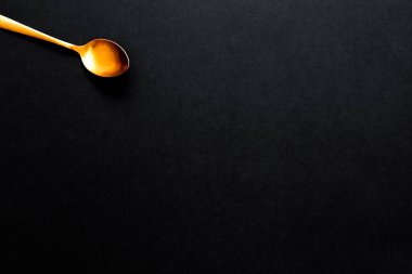 Bir köşede altın renkli çorba kaşığı, siyah arka planda, kopyalama alanı ile izole edilmiş..