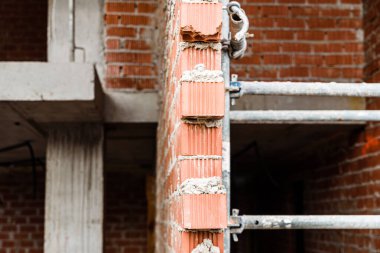 Metal yapı iskelesi kullanarak yeni bir yerleşim yerine duvar örmek için tuğlaları yapıştırmak için kullanılan beton kütlesi.