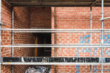 Metal yapı iskelesi kullanarak yeni bir yerleşim yerine duvar örmek için tuğlaları yapıştırmak için kullanılan beton kütlesi.