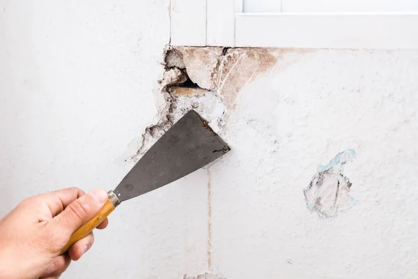 Applying white cement to a crack in a wall with a putty knife.
