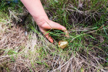 Bir kızın eli bahçesinde saklı çikolatalı paskalya yumurtaları toplar..