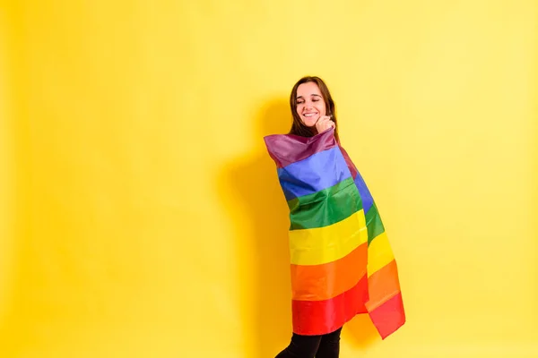 黄色の背景にLgbtの虹の旗を掲げた若い女性が — ストック写真