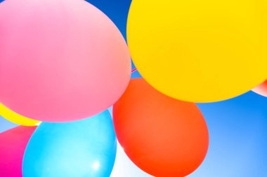 Aşağıdan mavi gökyüzü arkaplanlı oldukça güneşli katı renkli balonlar görünüyor