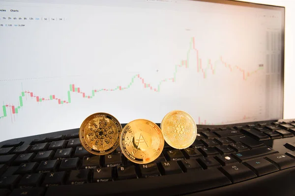Golden coins of ada cryptocurrencies, cardano coin, controlling the price on a monitor with graphs.