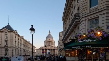 İnsanlar Pantheon 'u geçerken Paris' te bir restoranın önünde cadde boyunca yürüyorlar. Binalar akşam saatlerinde tarihi bir atmosfer yaratıyor..