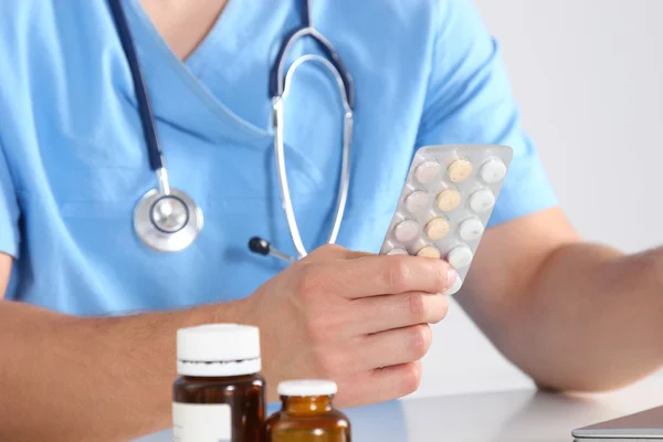 Médico sentado à mesa e segurando o frasco — Fotografia de Stock