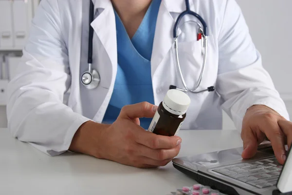 Médico sentado à mesa e segurando o frasco — Fotografia de Stock