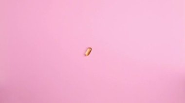Organik destek vitaminleri sarı kapsüller Omega 3 veya D-3 hapları pembe arka planda. Beslenme takviyesi üst görünümü