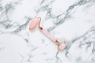 Mermer arka planda pembe Gua Sha masaj aleti, yakın plan. Rose Quartz yeşim taşı silindiri. Evde yüz bakımı, yaşlanma karşıtı ve kaldırma terapisi görüşü