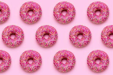 Pembe arka planda çok renkli serpiştirilmiş tatlı pembe donut üst görüş deseninde yatıyordu.