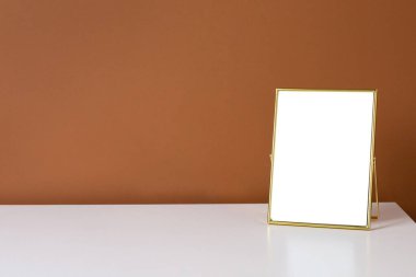 Koyu turuncu duvar arkaplan görünümlü beyaz masadaki altın çerçeve kopyalama alanı