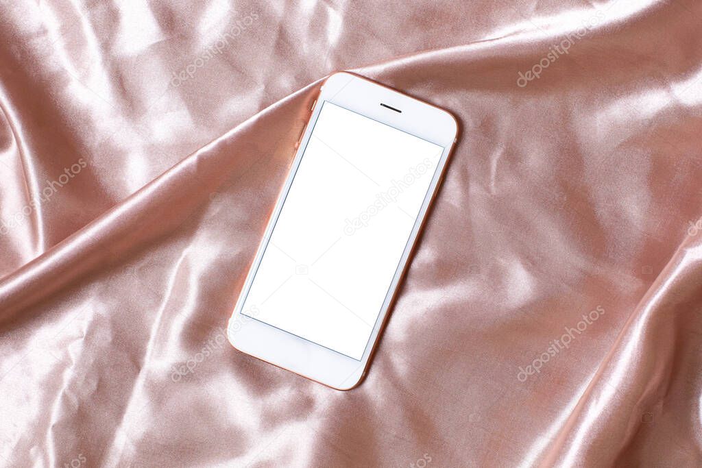 Flat lay concept of feminine light background with mobile phone on pink silk . Top view with copy space.