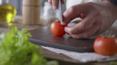 Aşçı ahşap mutfak tahtasına büyük mutfak bıçağıyla domates keser. Kırmızı domatesin doğrama görüntüsü. Sağlıklı beslenme konsepti. Diyet yemek. Yan görünümü kapat