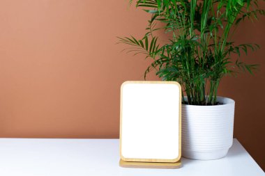 Ahşap çerçeve kopyalama alanı ve yeşil bitki beyaz masanın üzerinde koyu turuncu duvar arka plan görünümlü