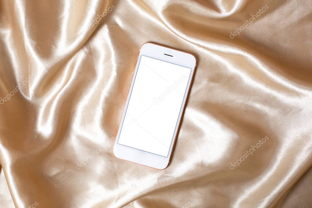 Flat lay concept of feminine light background with mobile phone on Beige silk .White screen with copy space top view.