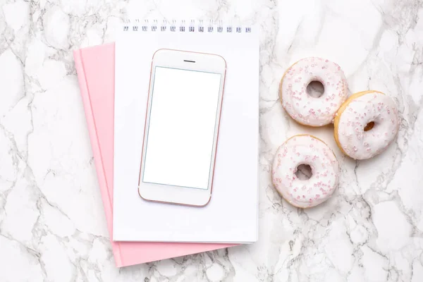 Mobile phone,pink notebook and sweet donut on a marble background flat lay, technology and sweet food top view